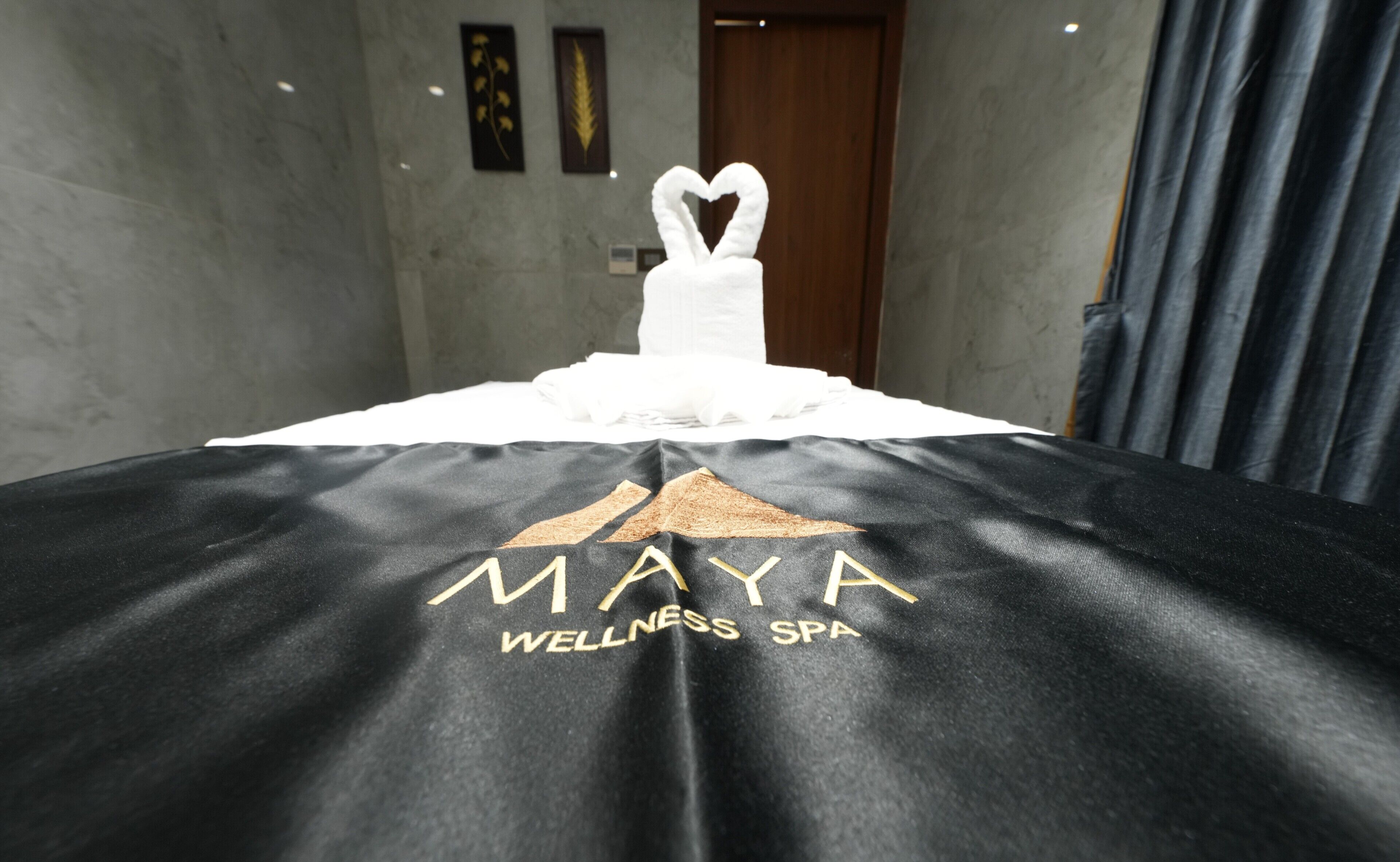 A bed with a towel shaped like a swan and a black sheet with 'MAYA WELLNESS SPA' text.