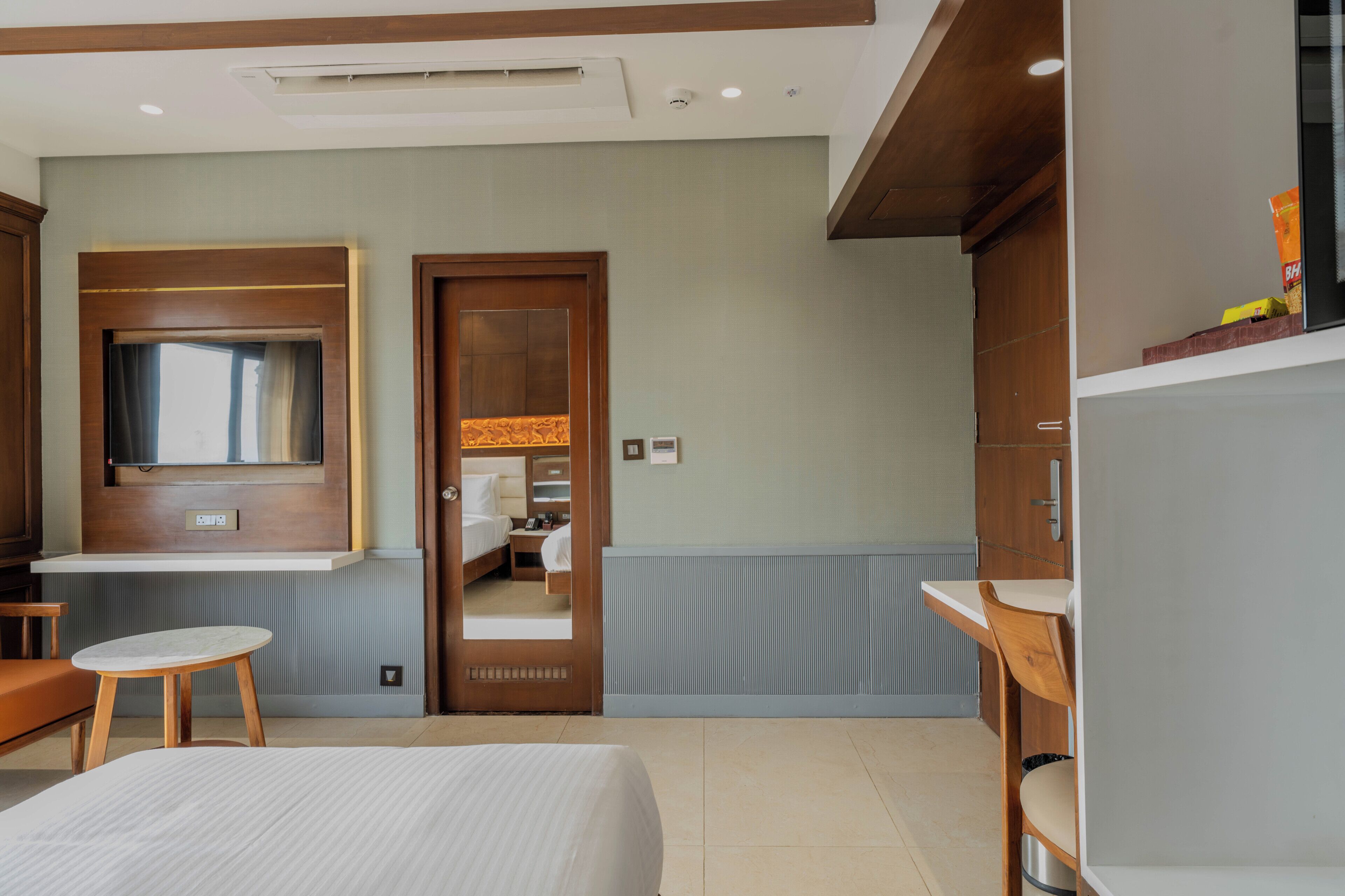 A hotel room with a bed, a desk, a chair, a TV, and a bathroom visible through an open door.