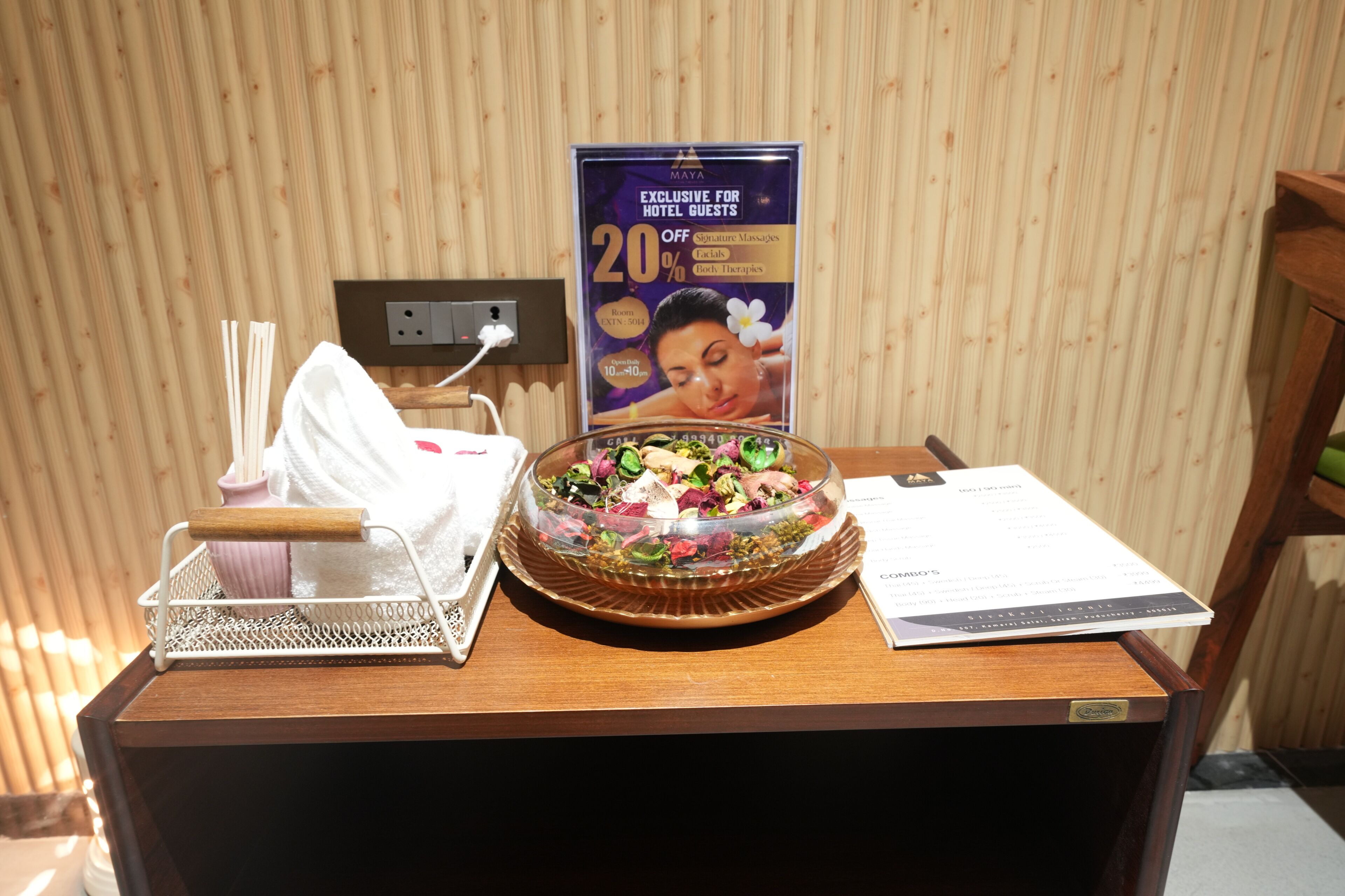 A wooden reception desk with a glass bowl of assorted fruits, a white tissue box, and a promotional sign for hotel guests.