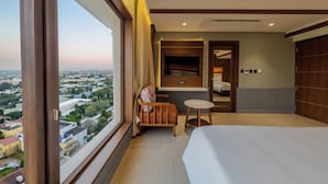 A hotel room with a large window, a bed, a small table, a chair, and a mirror. - SKI - Sivakavi Iconic (Puducherry)