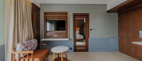 A hotel room with a sofa, a small round table, a mirror, a wooden cabinet, and a bathroom with a sink.