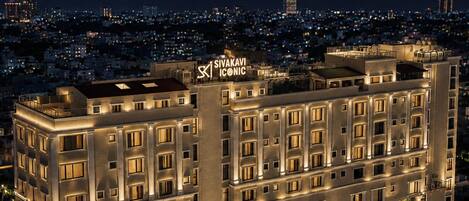 Un hôtel à plusieurs étages, reconnaissable à son enseigne bien visible où l’on peut lire « SIVAKAVI ICONIC ». Le bâtiment présente une façade symétrique, avec des fenêtres et des balcons régulièrement espacés.