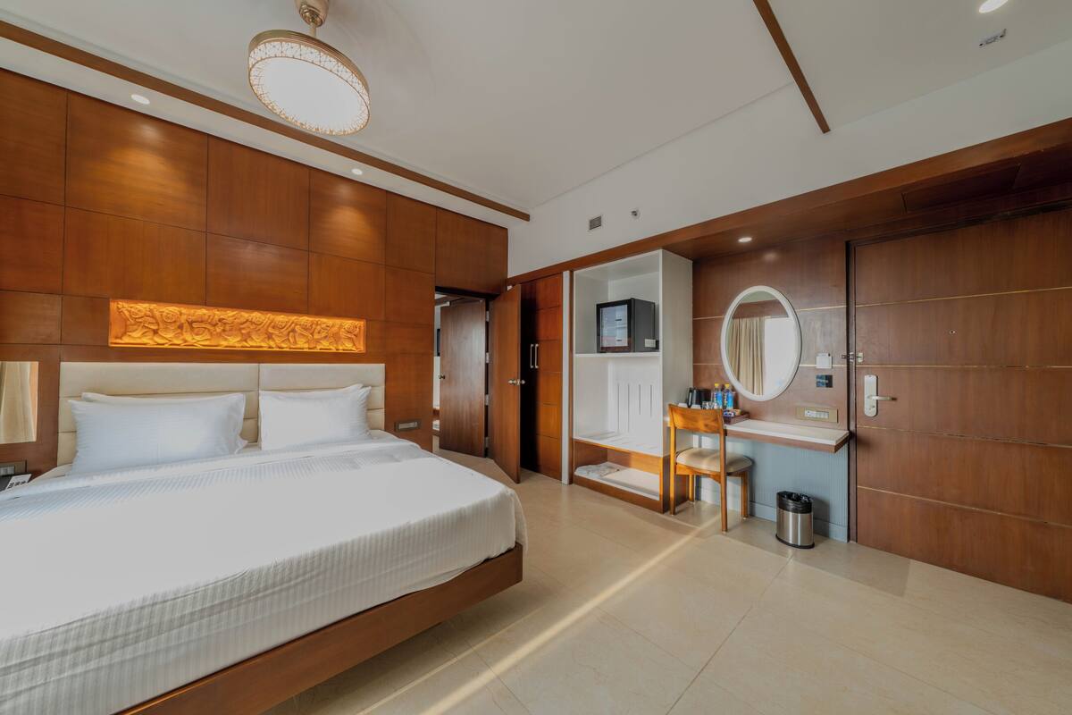 Una habitación de hotel moderna con una cama grande, un tocador con espejo, un escritorio pequeño y un vestidor.