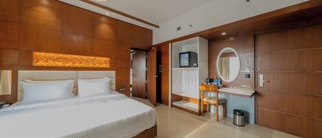 A modern hotel room with a large bed, a vanity with a mirror, a small desk, and a walk-in closet.