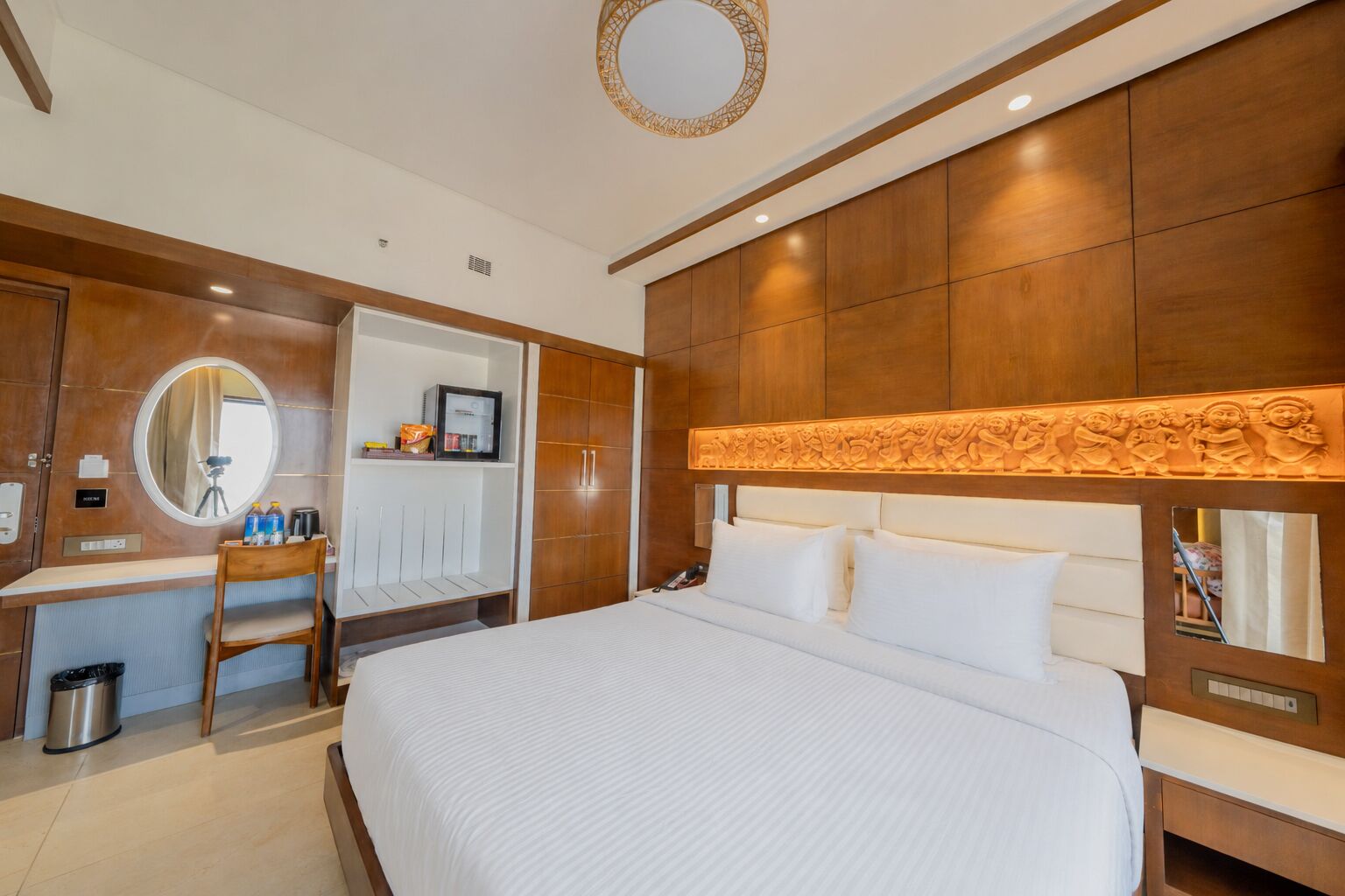A hotel room with a large bed, a desk with a chair, a wardrobe, and a mirror.
