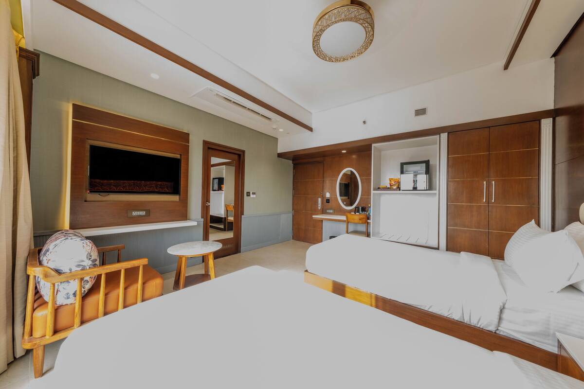 Una habitación de hotel moderna con una cama grande, un televisor montado en la pared, un armario de madera y un espejo redondo pequeño.
