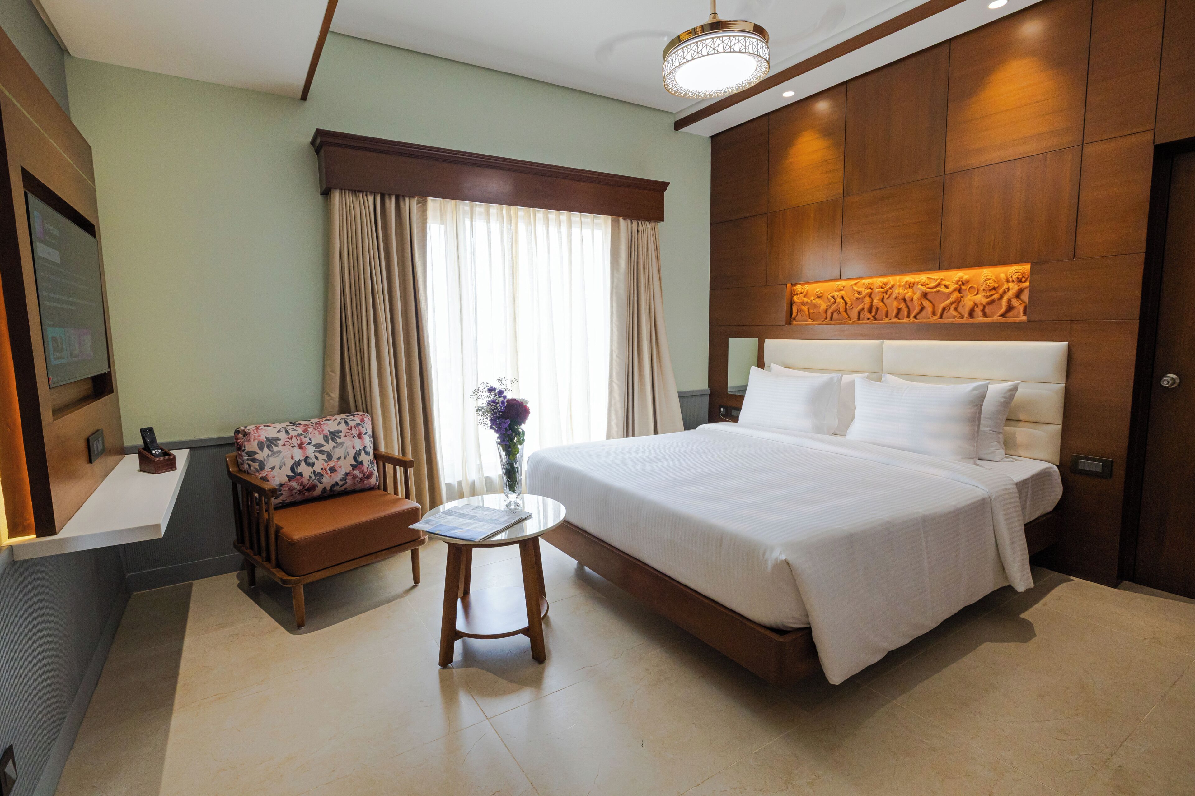 A hotel room with a large bed, a small table, a chair, a nightstand, and a wall-mounted artwork.
