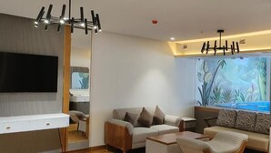 A modern living room with a flat-screen TV, a sofa set, a coffee table, and a large window with a tropical mural. - SKI - Sivakavi Iconic (Puducherry)