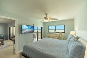 A bedroom with a bed, a ceiling fan, a TV, a dresser, and a window with a view of the beach. - Tropical Beachfront 2 Bed/2Bath Carlos Pointe Condo 131, White Sandy Beach (Fort Myers Beach)