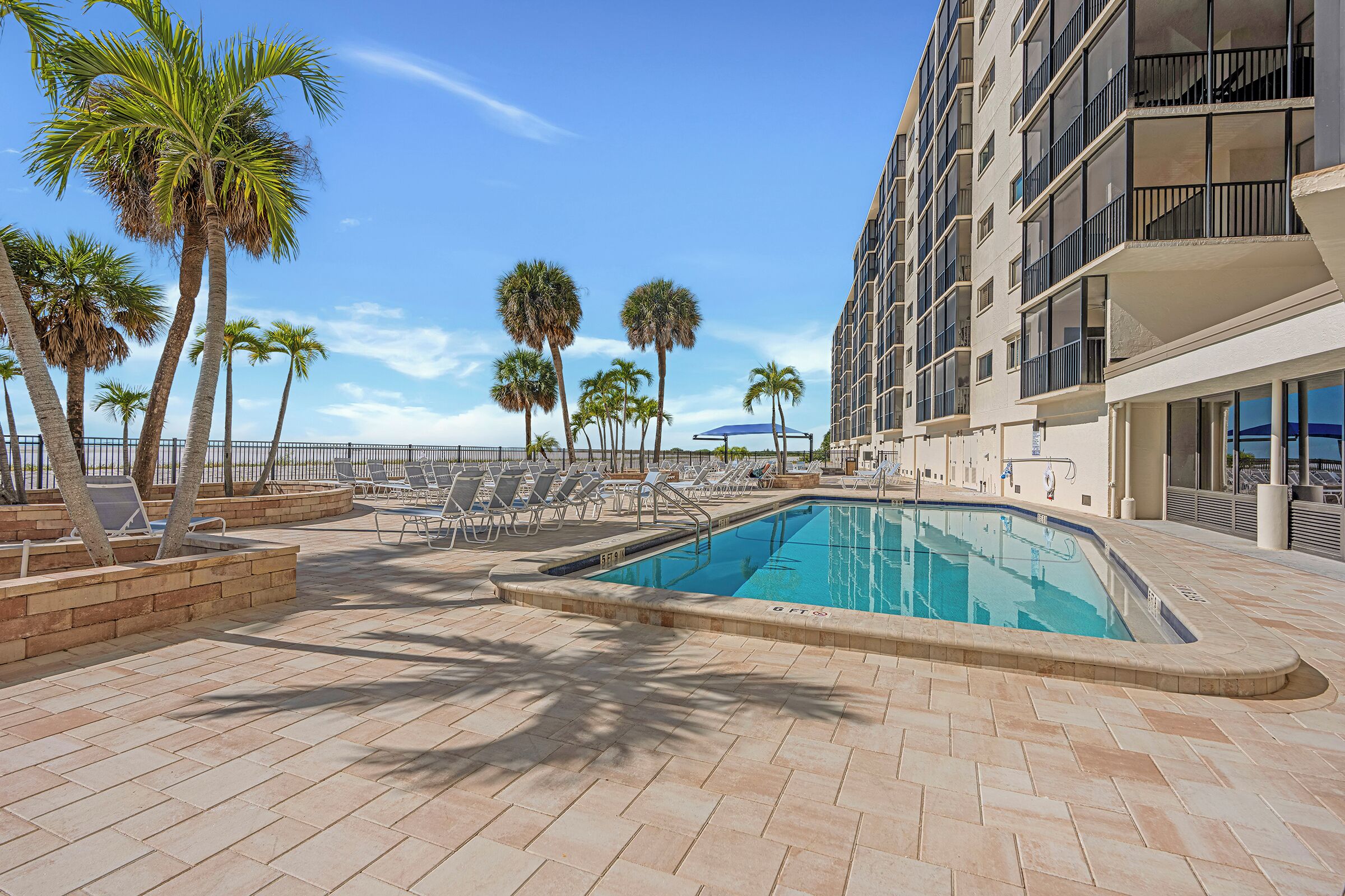 A swimming pool with lounge chairs and palm trees, surrounded by a building with balconies.