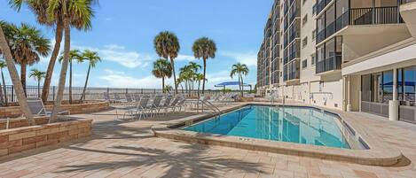 A swimming pool with lounge chairs and palm trees, surrounded by a building with balconies.