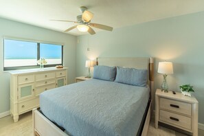 Un dormitorio con cama, mesitas de noche, cómoda, ventilador de techo y ventana con vistas.