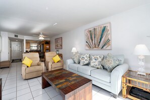 Ein Wohnzimmer mit einer Couch, Sesseln, einem Couchtisch und einem Essbereich im Hintergrund.