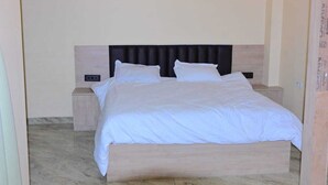A neatly made bed with a wooden headboard and two bedside tables. - Shree Videhi Atithi Grah (Samudrapur)