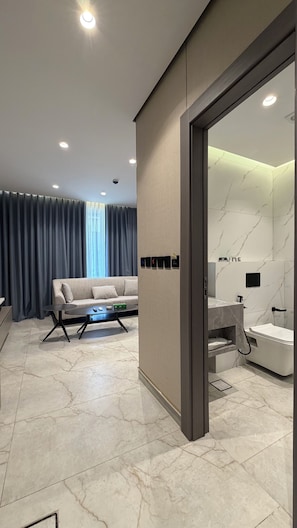 Ein modernes Wohnzimmer mit Sofa, Couchtisch und Blick auf ein Badezimmer mit Badewanne und Dusche.