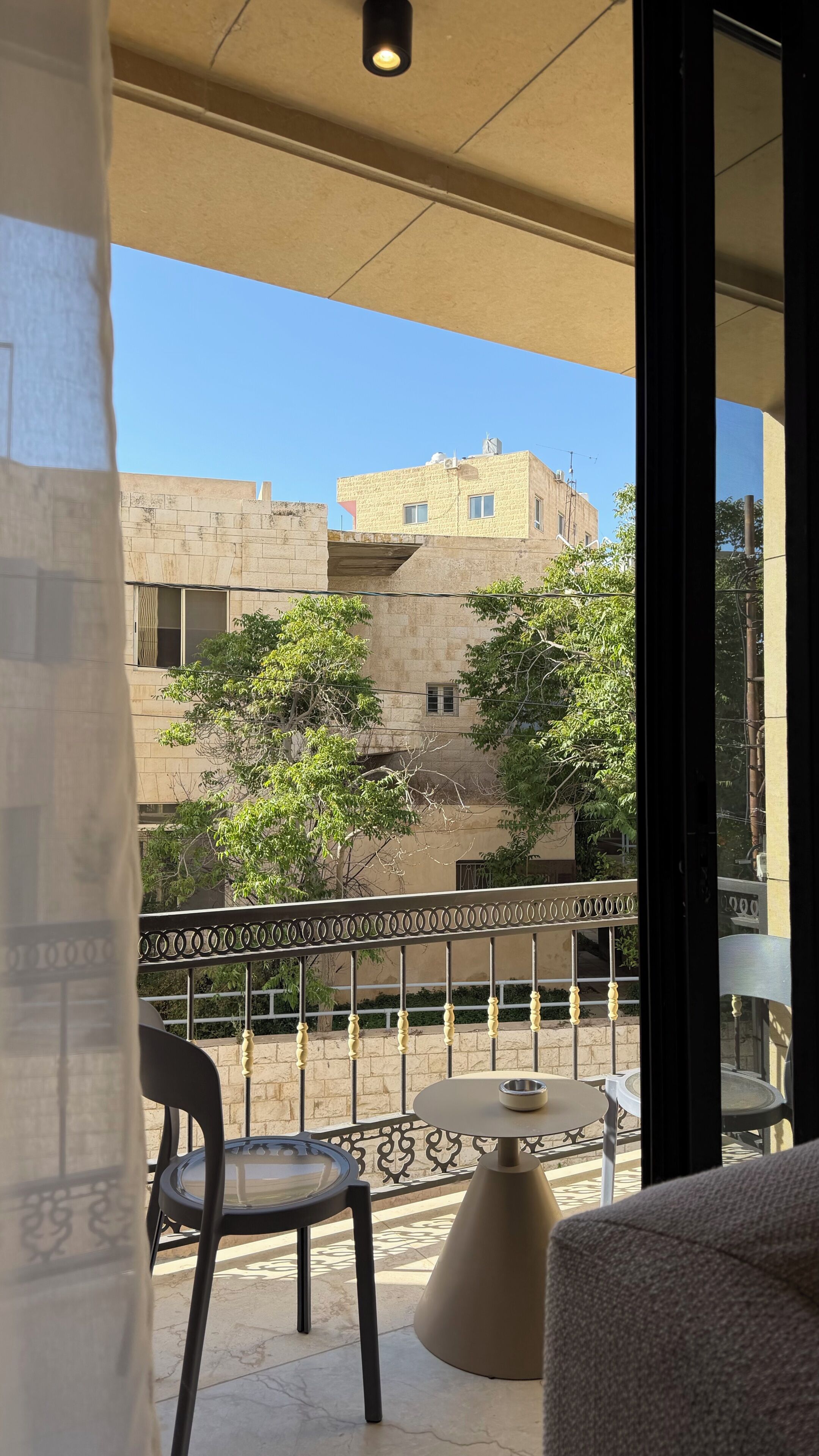 A balcony with a view of a building, a chair, a table, and a decorative railing.