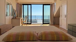 Ein Hotelzimmer mit einem großen Bett, einem Sessel, einem Schreibtisch und einem Balkon mit Blick.