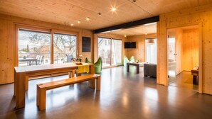 Une pièce spacieuse avec un plafond en bois, de grandes fenêtres, un banc en bois et une petite table.