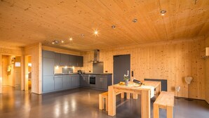 Une cuisine moderne avec des murs en bois et un îlot central, un coin repas avec une table et des bancs en bois, et un évier de cuisine visible.