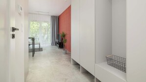 Een moderne hotelkamer met een minimalistisch design, met een witte kast, een rode accentmuur, een kleine plant en een mandje op een plank.