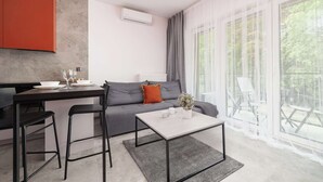Een moderne leefruimte met een keukenhoek, een grijze bank, een salontafel en een eettafel met stoelen.