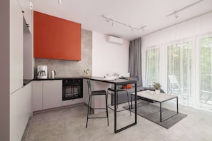 A modern kitchen with a dining area, featuring a kitchen island, bar stools, and a view of greenery through large windows. - Unique Studio for 2 People | Spacious Balcony (Katowice)