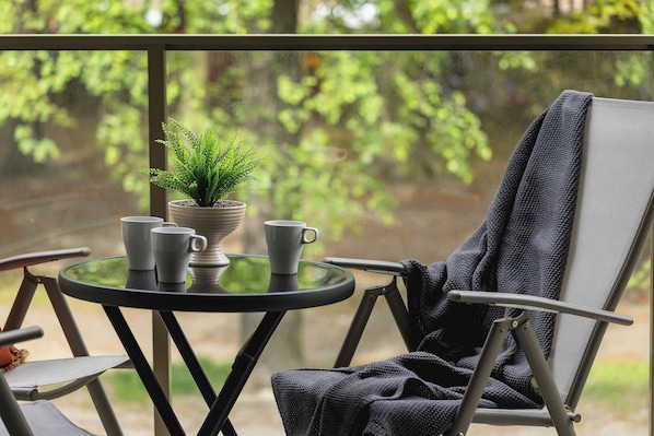 A balcony with a table, chairs, a potted plant, and a window with a view of greenery. - Unique Studio for 2 People | Spacious Balcony (Katowice)