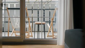 A room with a large sliding glass door leading to a balcony with a view of buildings and bare trees. There are two easels and a small stool on the balcony. - Muskatellerhaus Holiday Home with Shared Pool, Private Terrace, and Wi-Fi (Auggen)