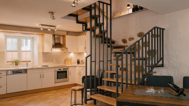 A modern kitchen with a wooden staircase, a dining area, and a view of the city. - Muskatellerhaus Holiday Home with Shared Pool, Private Terrace, and Wi-Fi (Auggen)