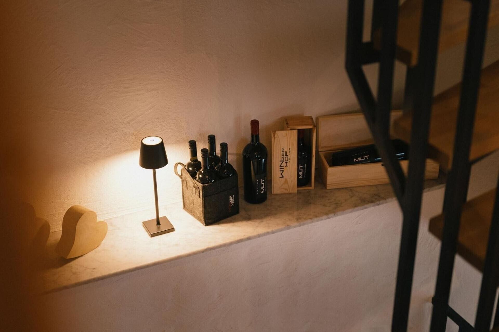 Un meuble à bouteilles contenant des bouteilles et des caisses, placé sur une étagère, une lampe et un escalier.