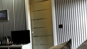 A hotel room with a bed, a TV, a coffee maker, and a door with striped wallpaper.