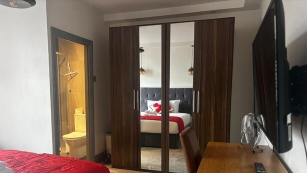 A hotel room with a bed, a desk, a mirror, a wardrobe, and a sliding door leading to a bathroom.