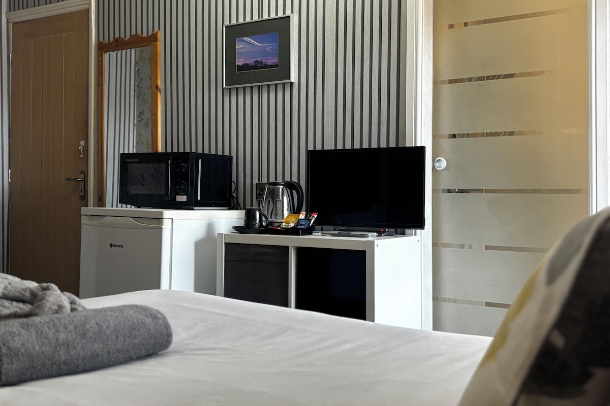 Habitación de hotel con cama, microondas, televisión y cafetera sobre una mesita.