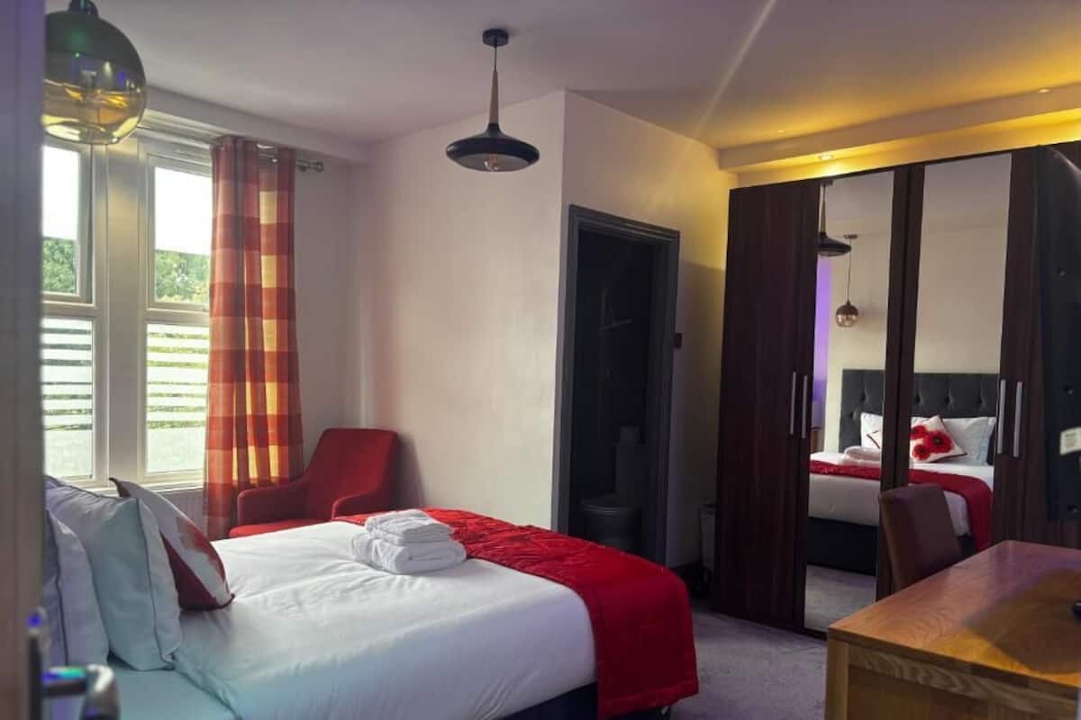 A hotel room with a bed, a desk, a chair, a wardrobe, and a door leading to another room.