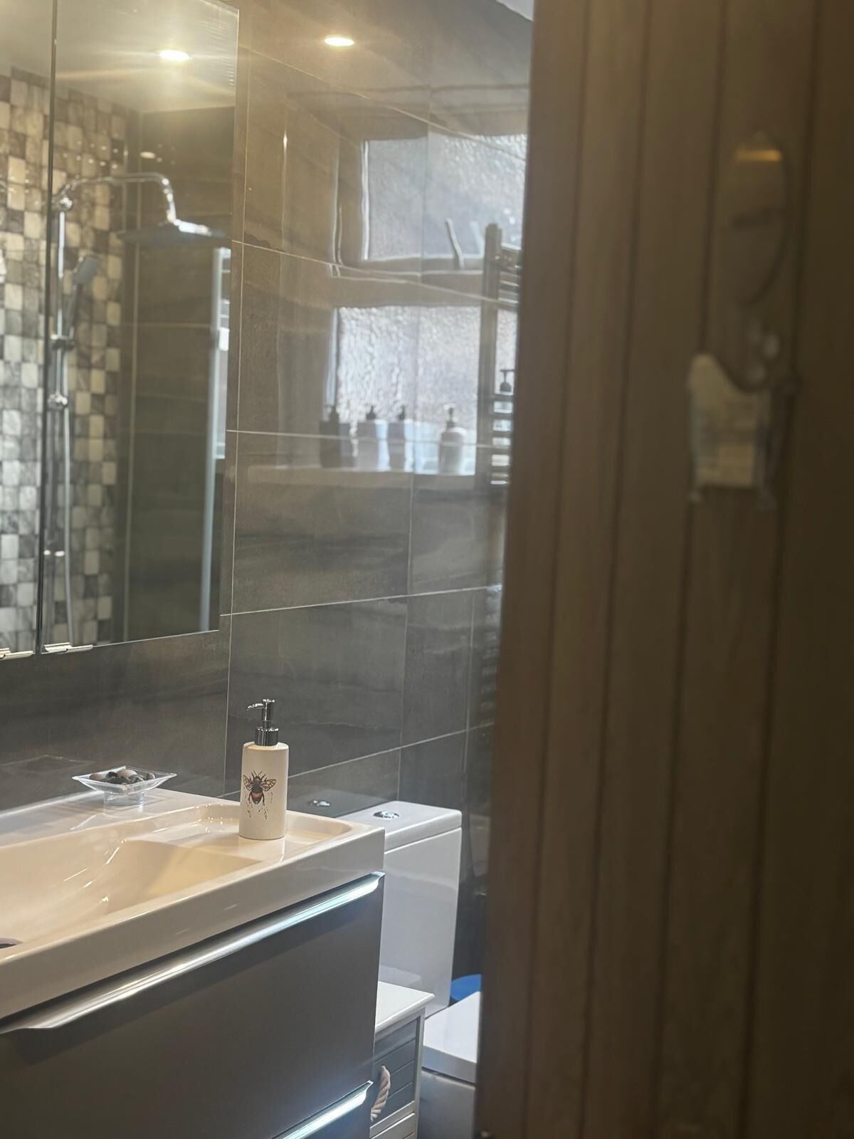 A bathroom with a large mirror, a sink, a shower, and a toilet.