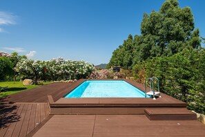 Ein Schwimmbecken mit Holzterrasse, umgeben von üppiger Vegetation und Bäumen.