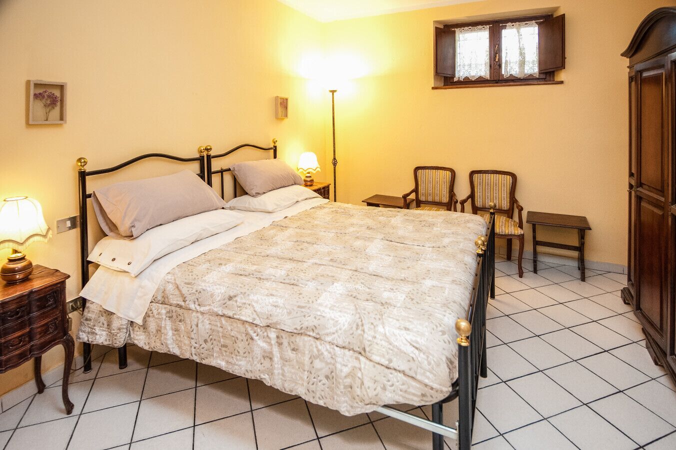Un dormitorio con cama, mesita de noche, lámpara, sillas y una ventana.