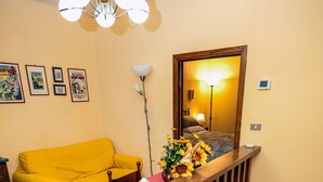 Un salon avec un canapé jaune, une table à manger recouverte d’une nappe rouge et un escalier doté d’une rampe en bois.