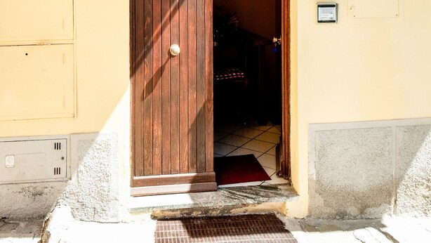 Une entrée d’immeuble avec une porte en bois, une petite marche menant à l’intérieur et un sol carrelé.