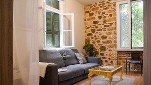 A living room with a grey sofa, a wooden coffee table, a stone wall, and a window with shutters. - Kerameikos Radio-Apartments (Athina)