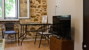 A room with a stone wall, a window, a TV, a wooden dresser, and two chairs. - Kerameikos Radio-Apartments (Athina)