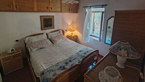 Une chambre à coucher comprenant un lit, une armoire en bois, une table de chevet, une lampe et une fenêtre avec des rideaux.