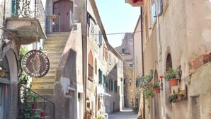 Une rue étroite avec des terrasses, des bâtiments en pierre et un escalier menant à une porte.