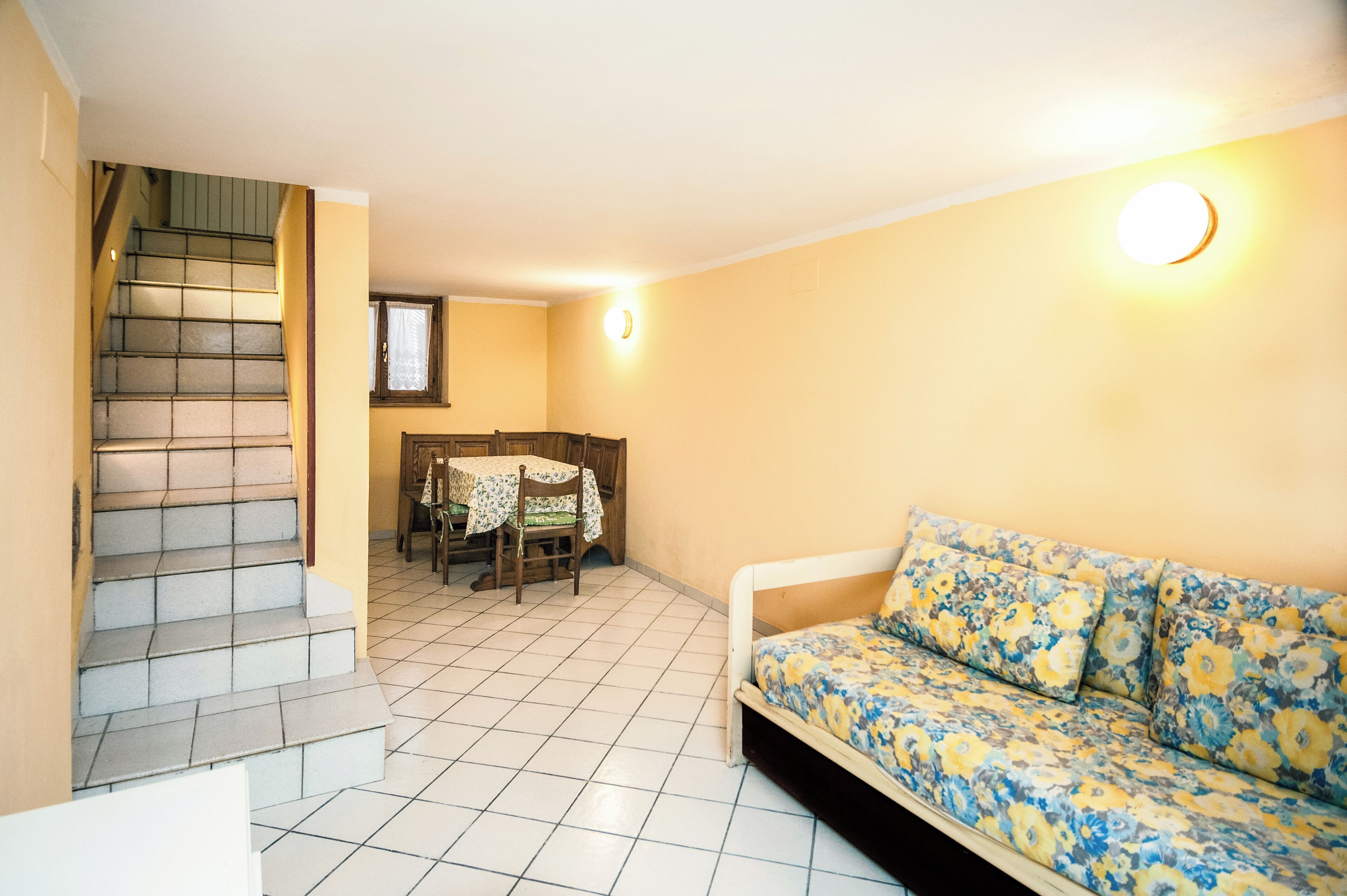 A room with a sofa, a dining table with chairs, and a staircase.
