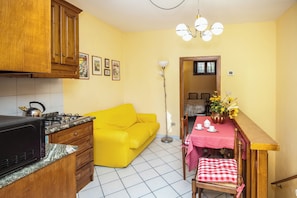Una cocina compacta con un sofá amarillo, una mesa de comedor con mantel rojo y una escalera de madera.