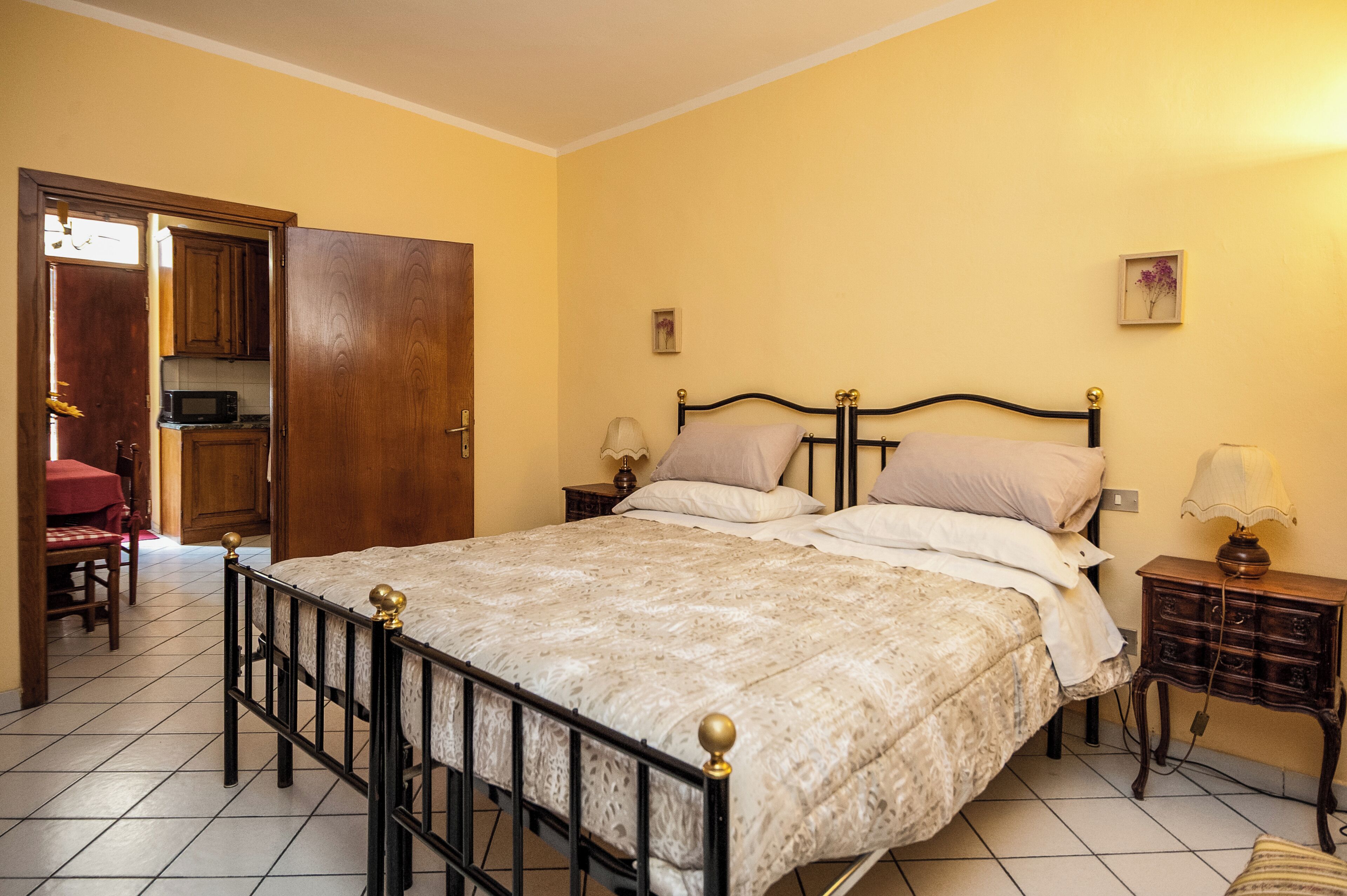 Un dormitori amb llit, una tauleta de nit, una làmpada, una porta de fusta i una zona de cuina.