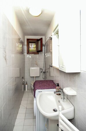 A narrow bathroom with a toilet, sink, and shower. - Casina Travi (Arezzo)