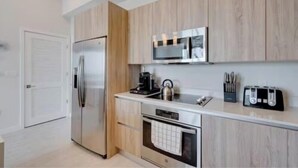 A modern kitchen with wooden cabinets, stainless steel appliances, and a countertop with a kettle and utensils. - Luxury 1 Bedroom Condo with Free Parking (Miami)