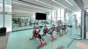 A gym with exercise equipment, a large mirror, and a television screen. - Luxury 1 Bedroom Condo with Free Parking (Miami)