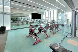 Ein Fitnessstudio mit Trainingsgeräten, einem großen Spiegel und einem Fernsehbildschirm.